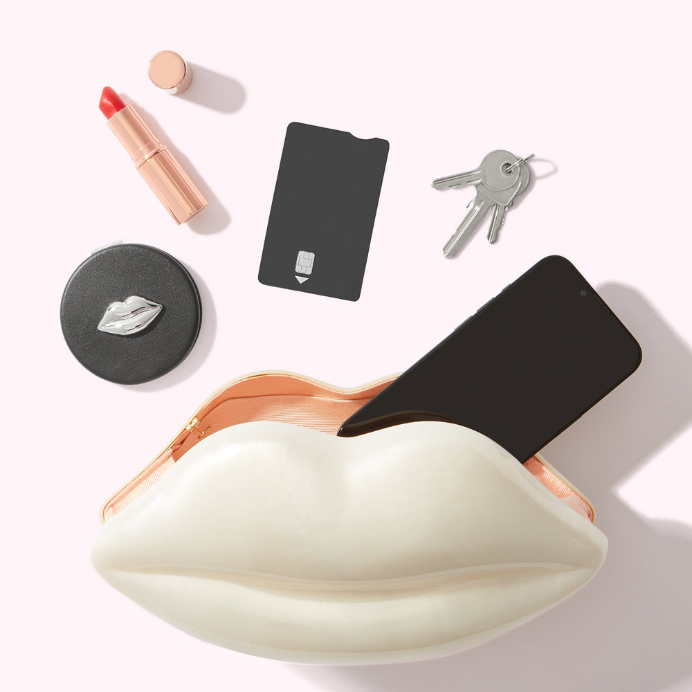 A white lip-shaped purse on a white background containing a smartphone, lipstick, compact mirror, credit card, and keys.