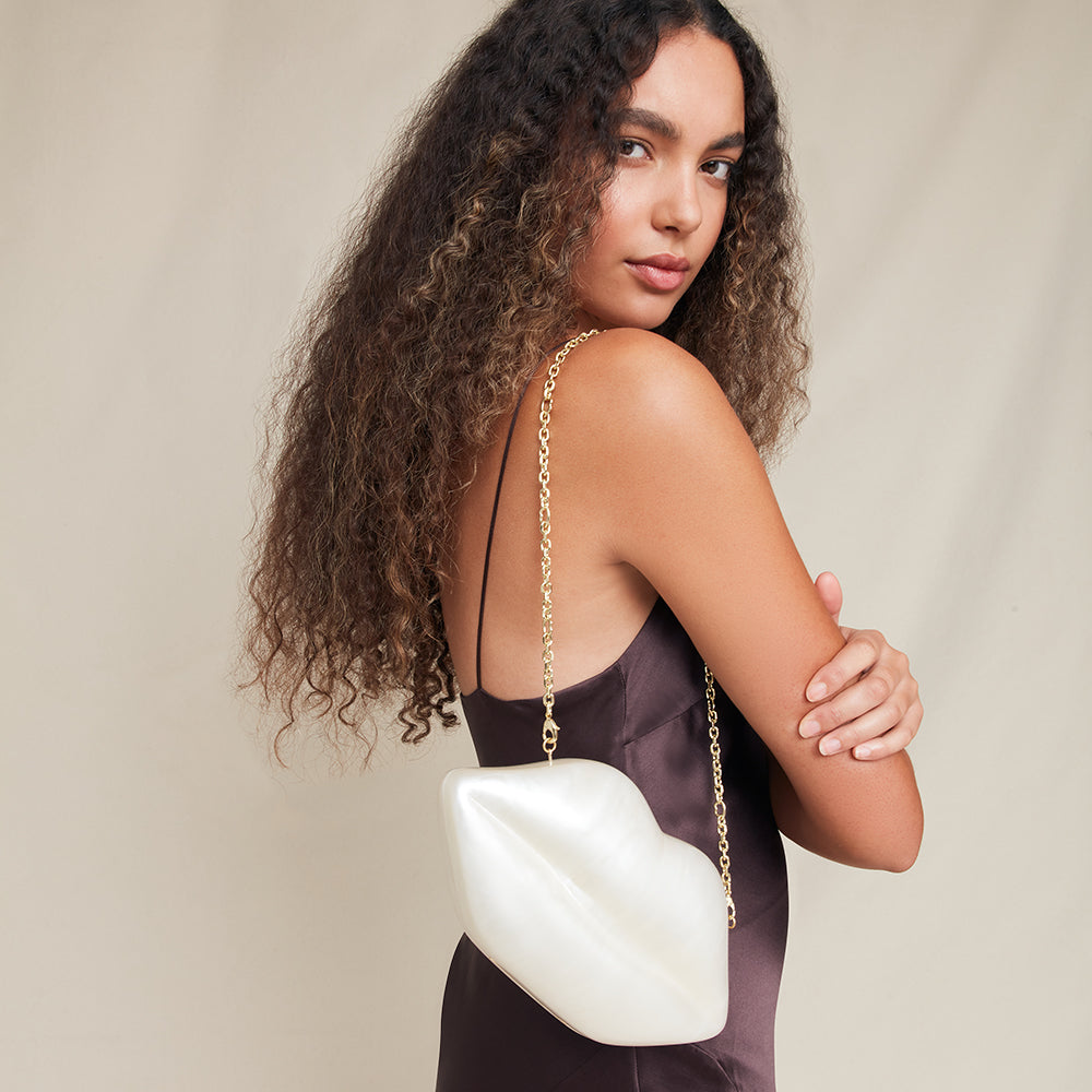 Woman holding a white lip shaped handbag with a gold chain strap against a beige background