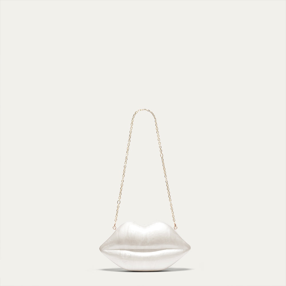 White pearl lip shaped clutch with a gold chain shoulder strap on a light gray background