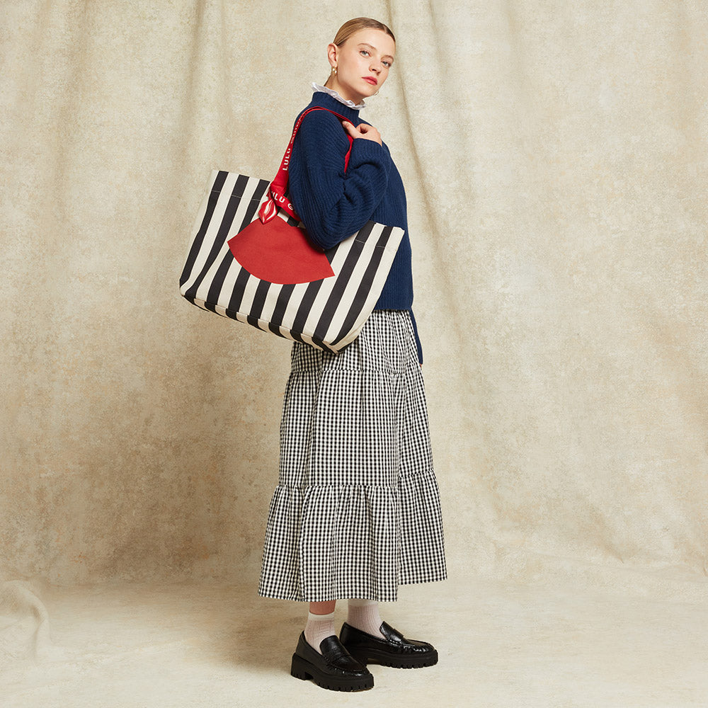 Woman holding a black and beige striped tote bag with a red lip printed on the front against a beige background