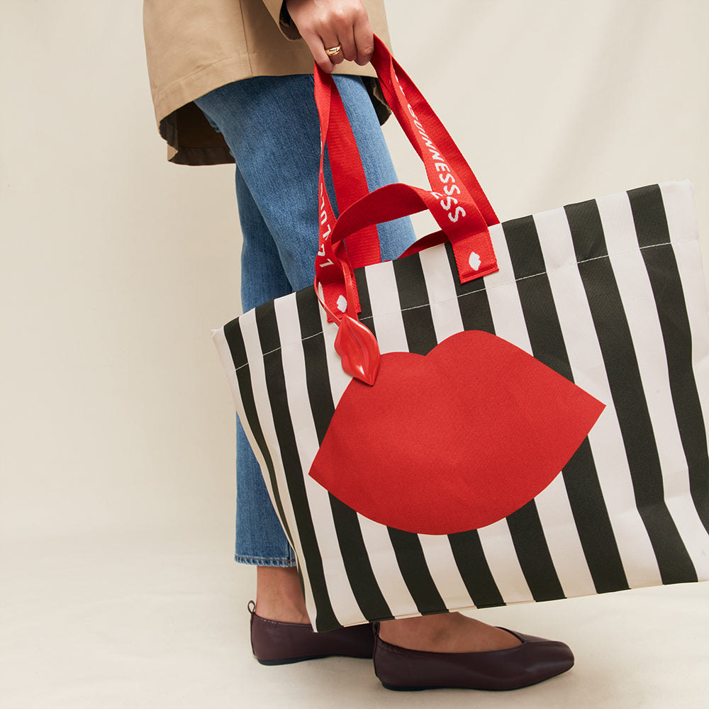 Tote bag with red lips and black and white stripes held by a person.