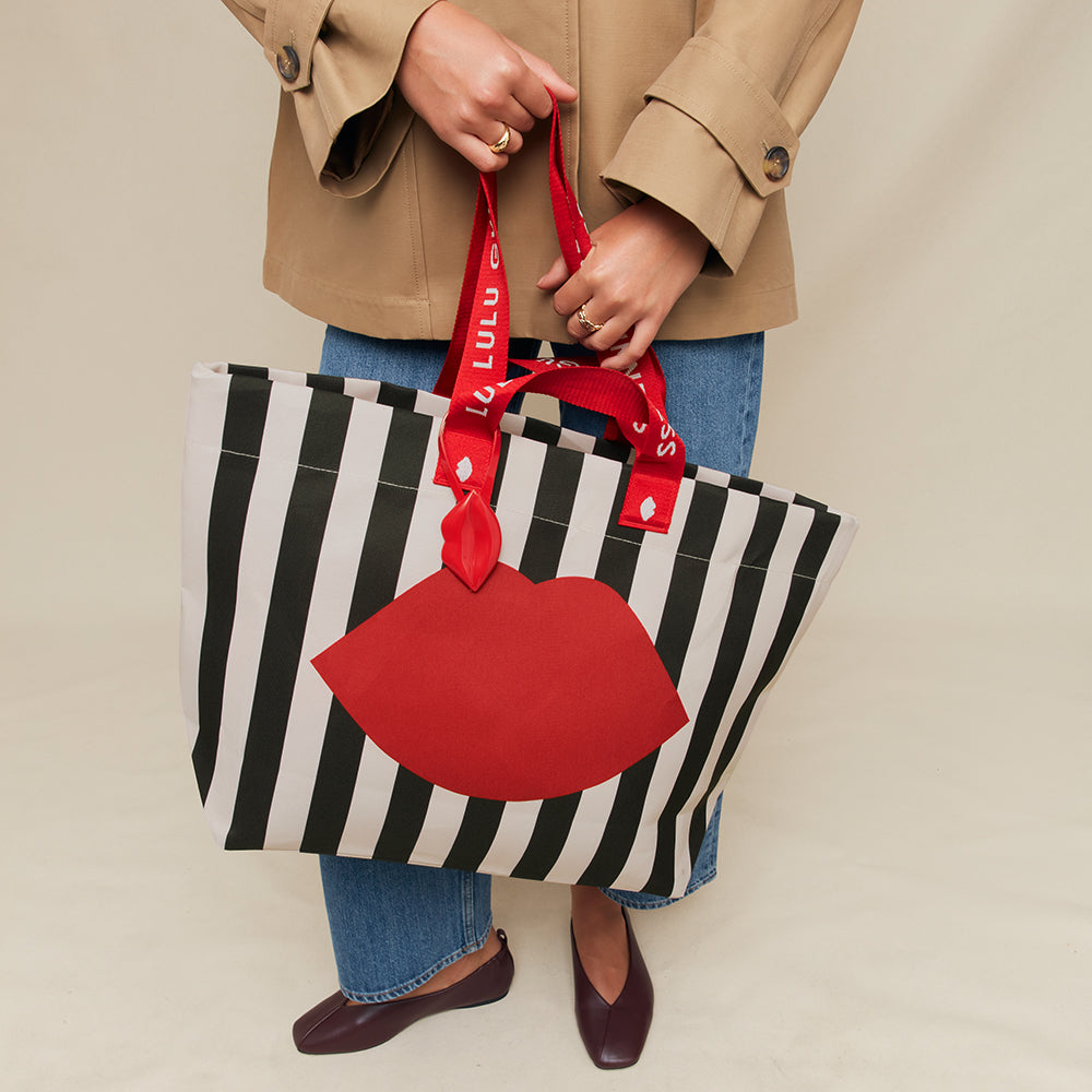 Person holding a black and white striped tote bag with a red lip design and a matching red strap.