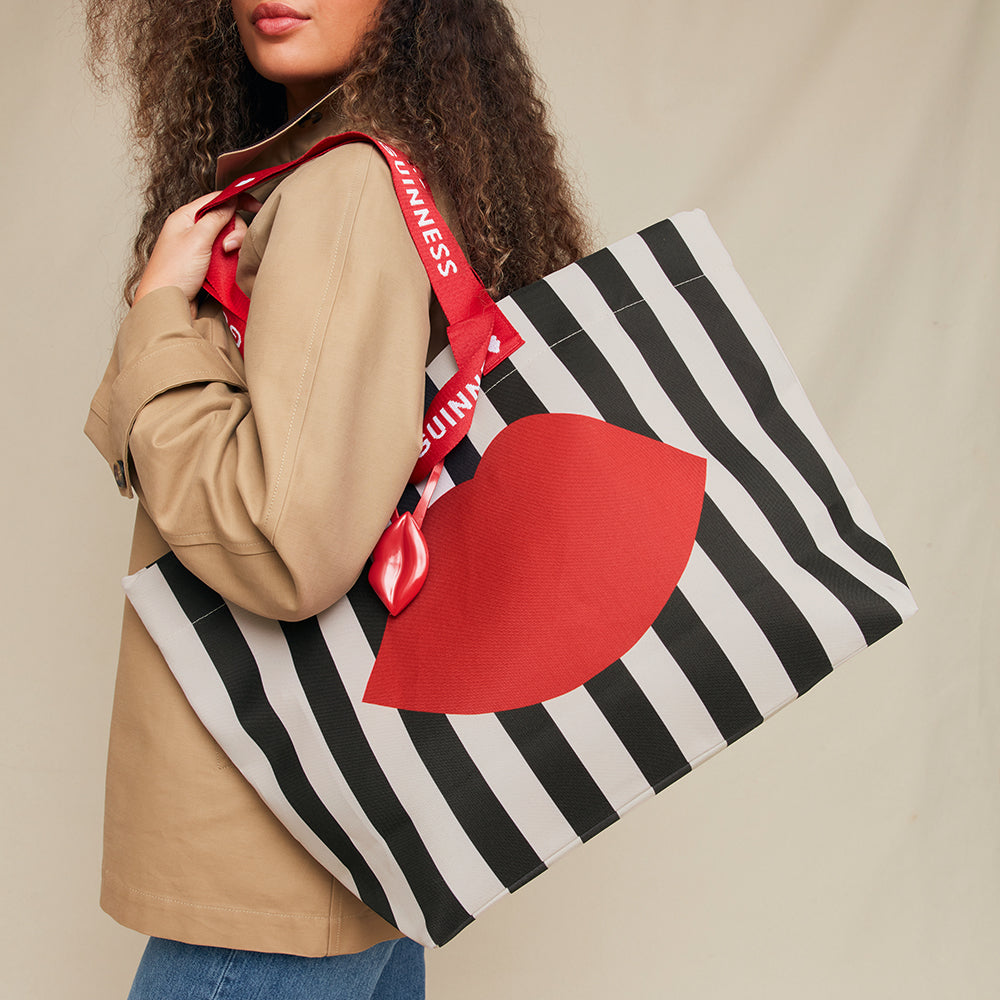 Person holding a black and white striped tote bag with a red lip and 'LULU GUINNESS' branding.