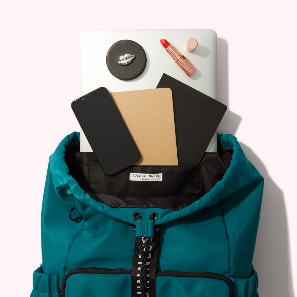Teal Lulu Guinness backpack with laptop, phone, notebooks, lipstick, and compact mirror inside.
