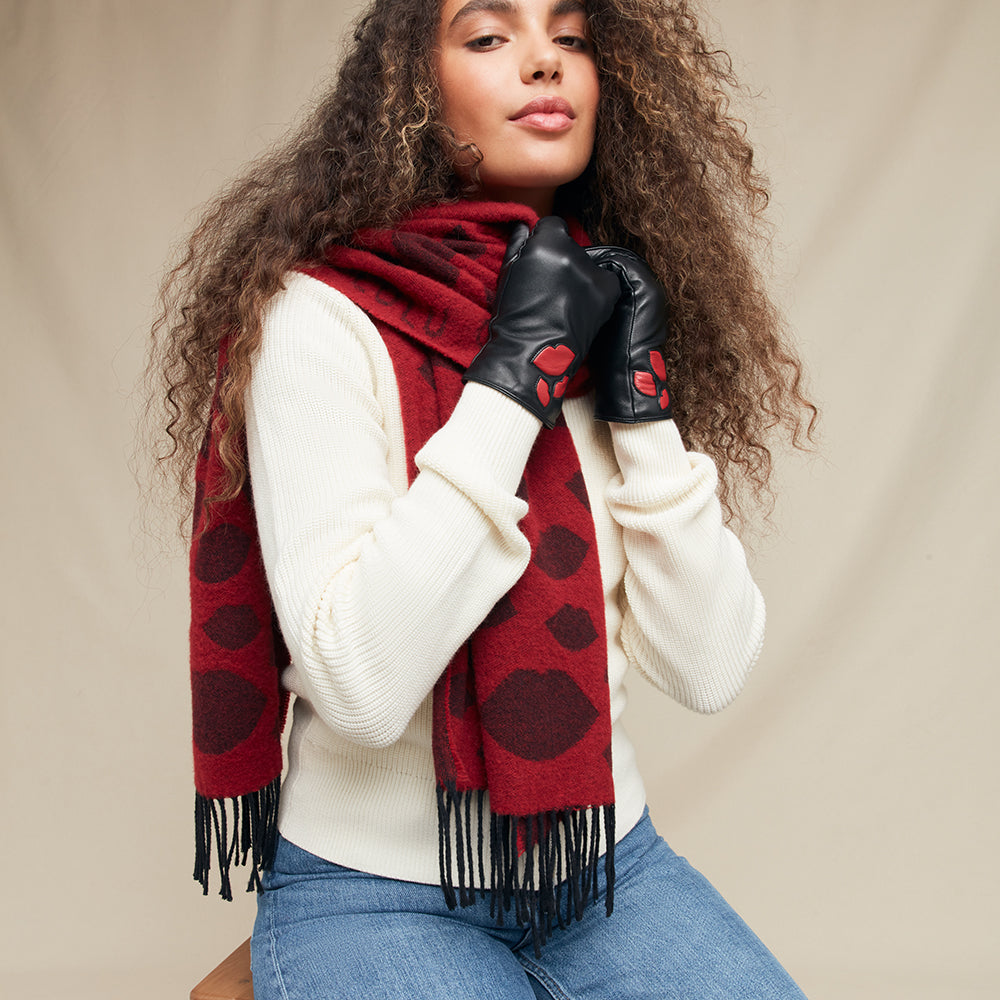 Woman wearing a red wool scarf and a pair of black leather gloves with lip detailing against a beige background