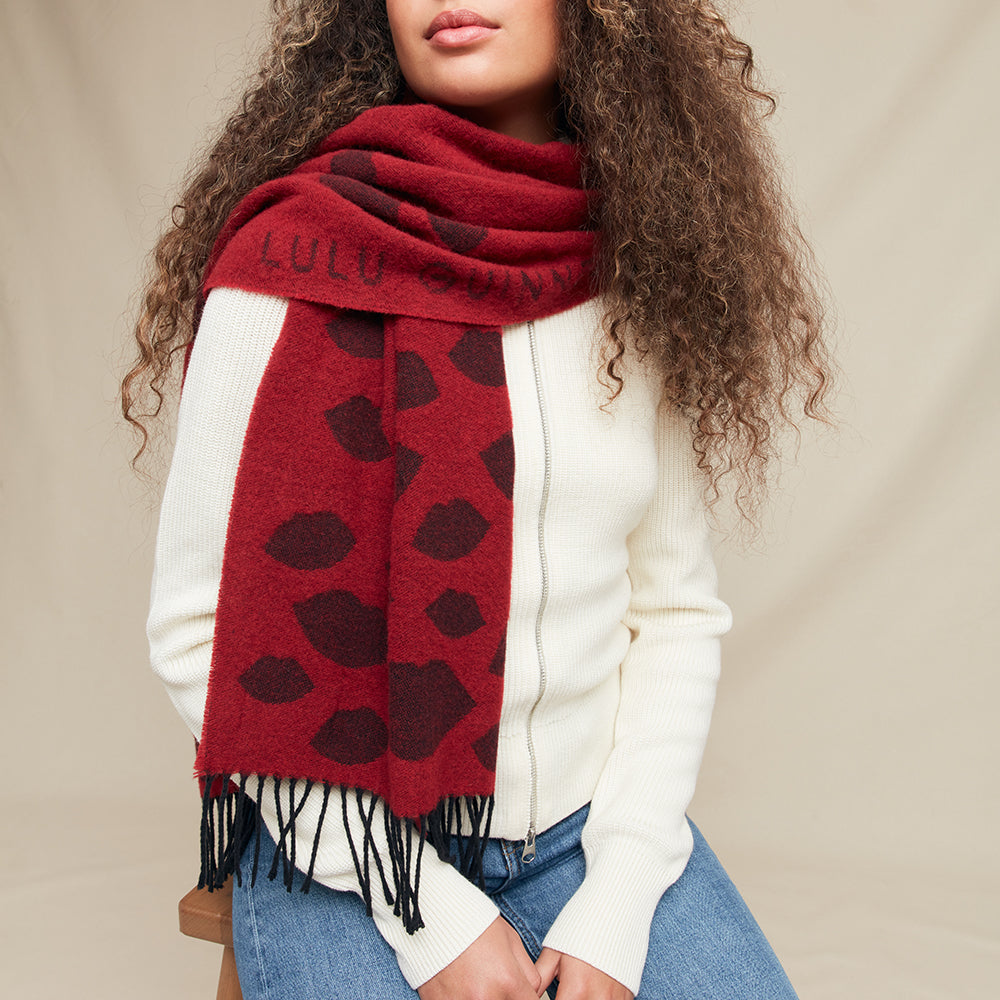 Women wearing a red scarf with black lip detail and 'Lulu Guinness' logo against a beige background