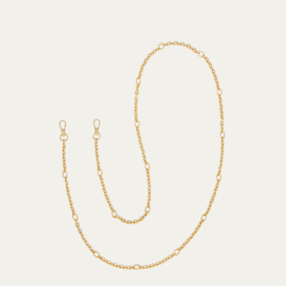 A delicate gold chain accessory with alternating small oval links and larger lip-shaped links, displayed on a light cream background.