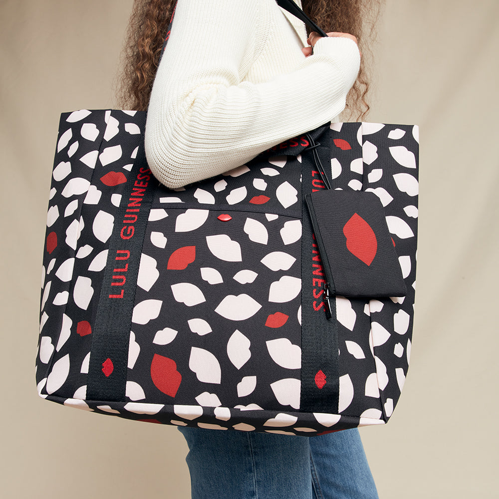 Person holding a black tote bag with red and white pattern, featuring 'Lulu Guinness' branding.
