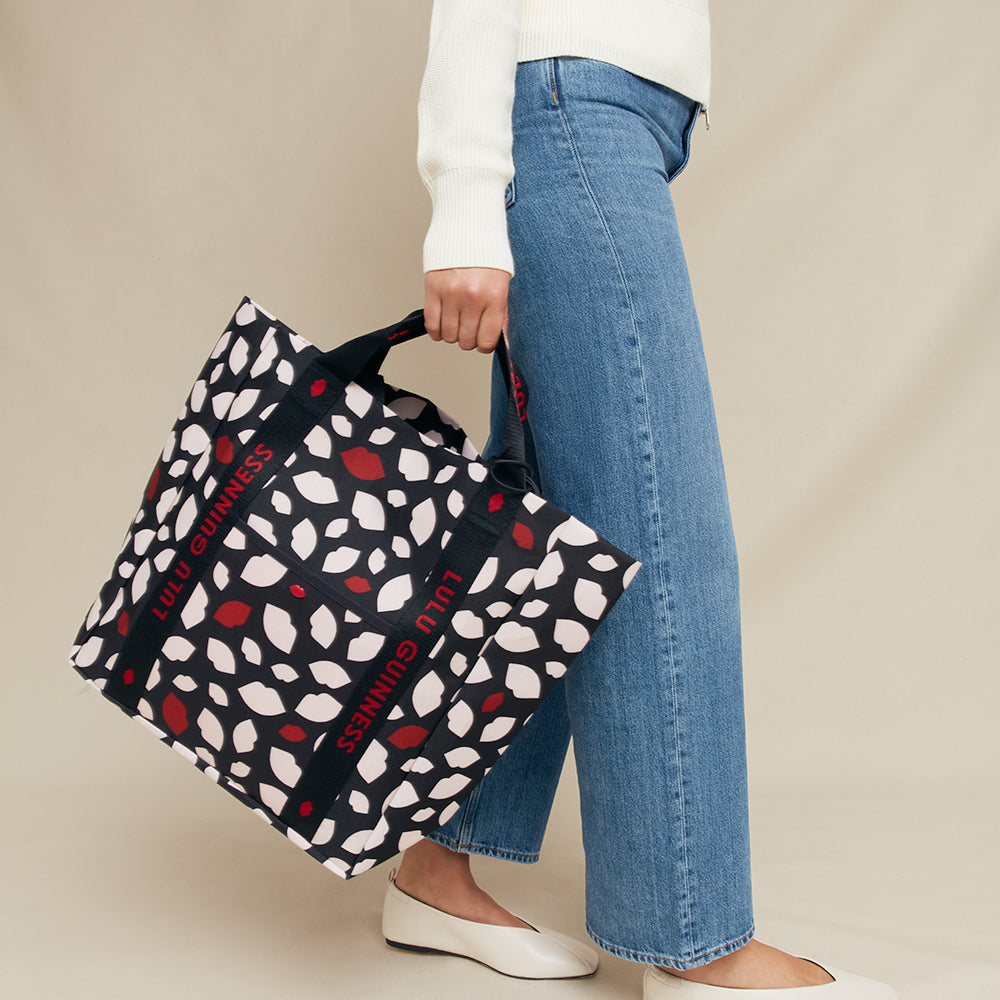 Person holding a lip patterned bag with visible branding against a beige background