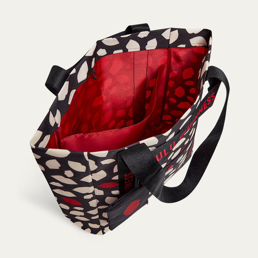 Tote bag with black, red, and which lip flurry print, open to reveal a red lining and inside pocket on a white background