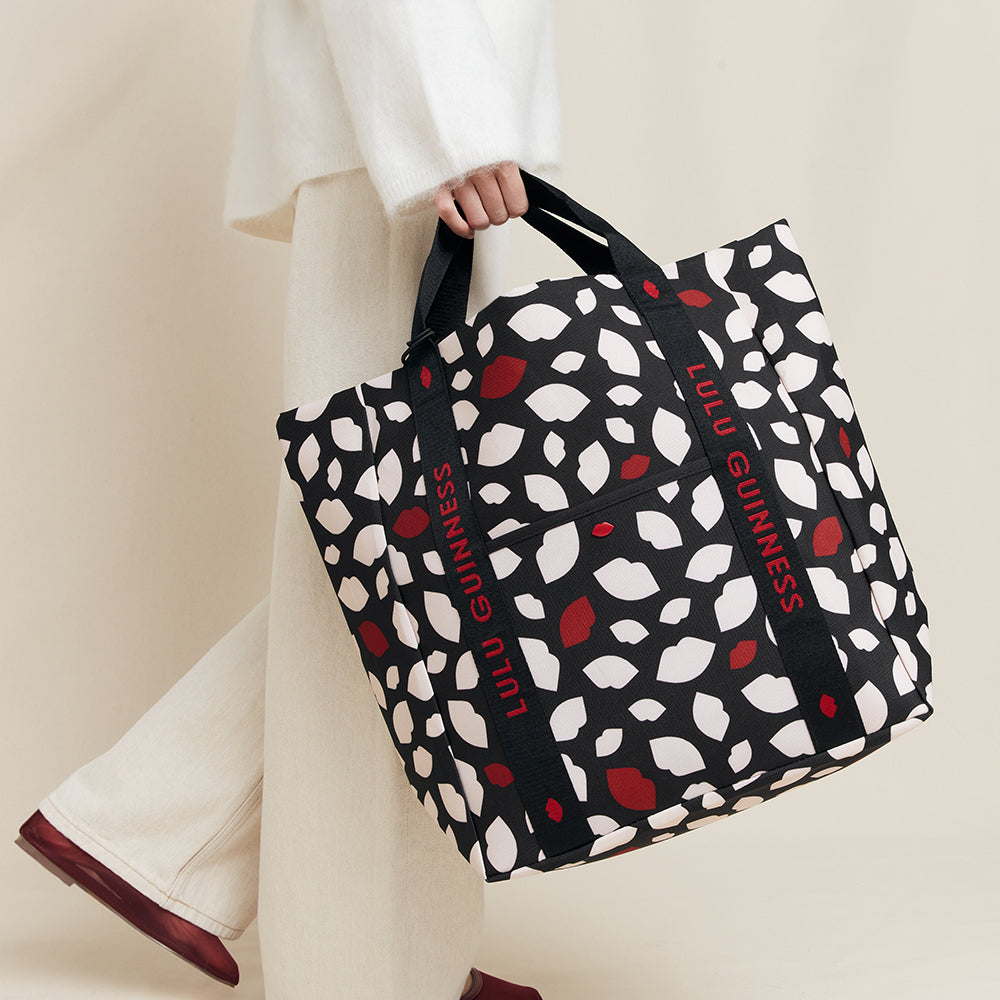 Person holding a Lulu Guinness lip print tote bag with a black, white, and red pattern.