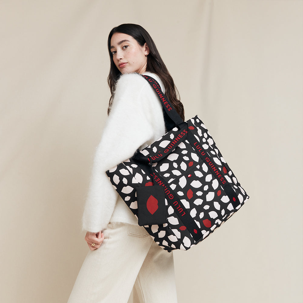 Woman carrying a lip print patterned tote bag with visible 'Lulu Guinness' branding against a plain background