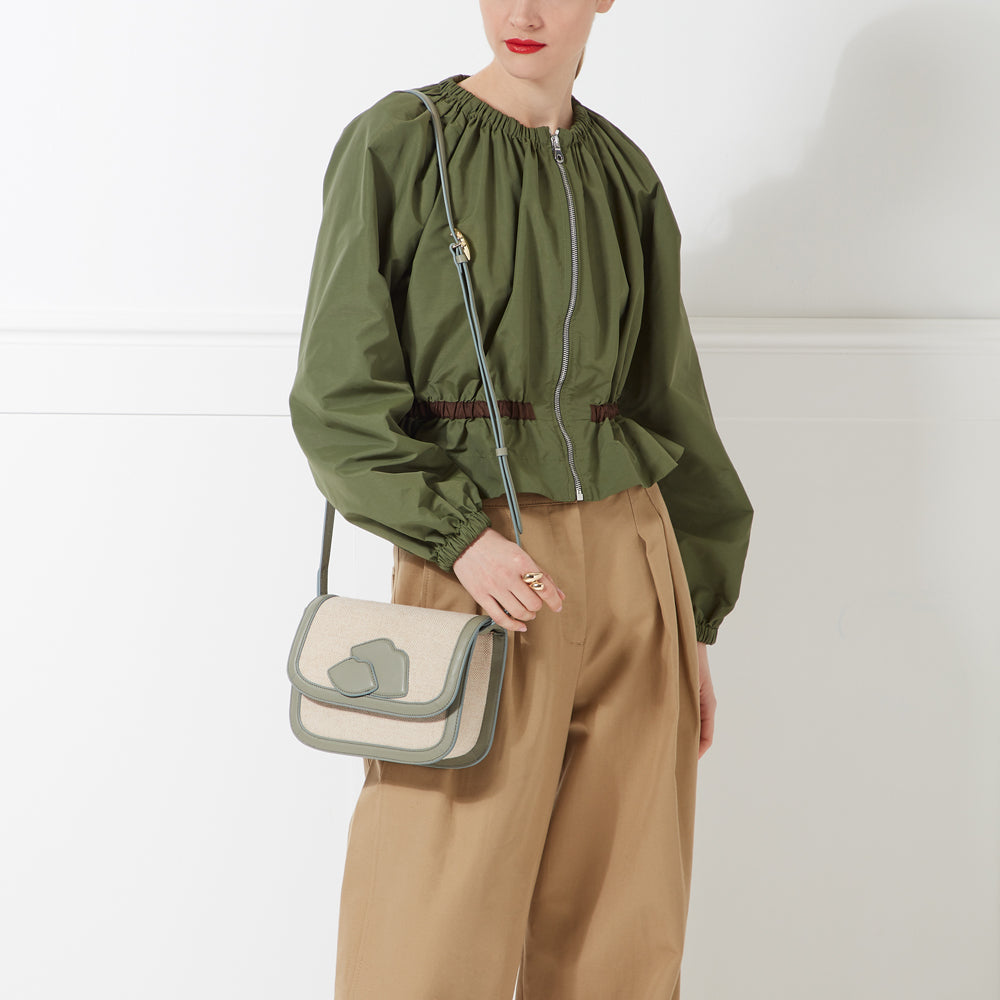 Woman in olive green zip-up top and khaki pants carries a sage green and beige crossbody bag.
