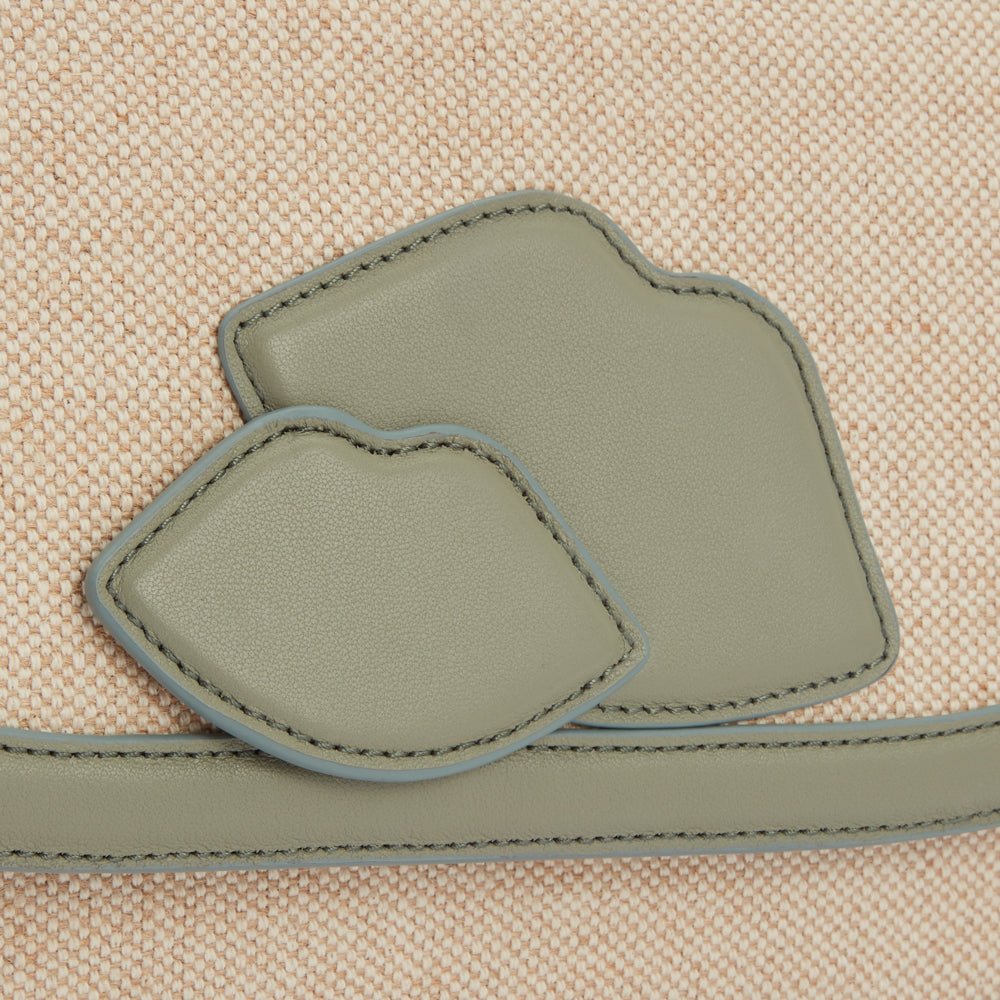 Close-up of a beige canvas bag with two olive-green leather lip appliqué and a matching trim.
