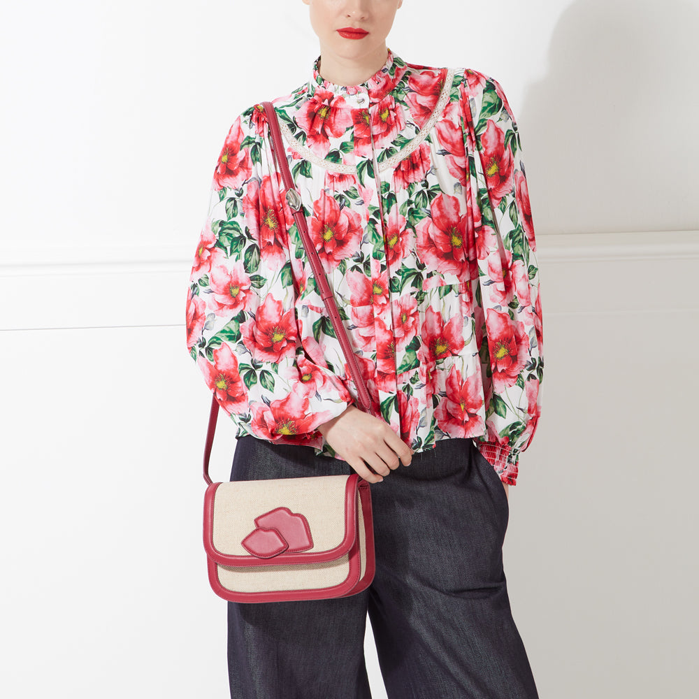 Woman wearing a floral blouse and dark pants, carrying a red and beige crossbody bag.
