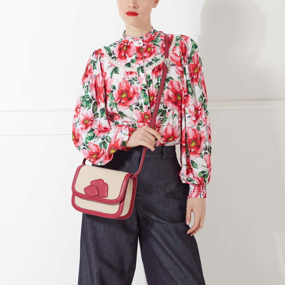 Woman wearing a red and white floral blouse and dark denim pants, carrying a red and beige crossbody bag.