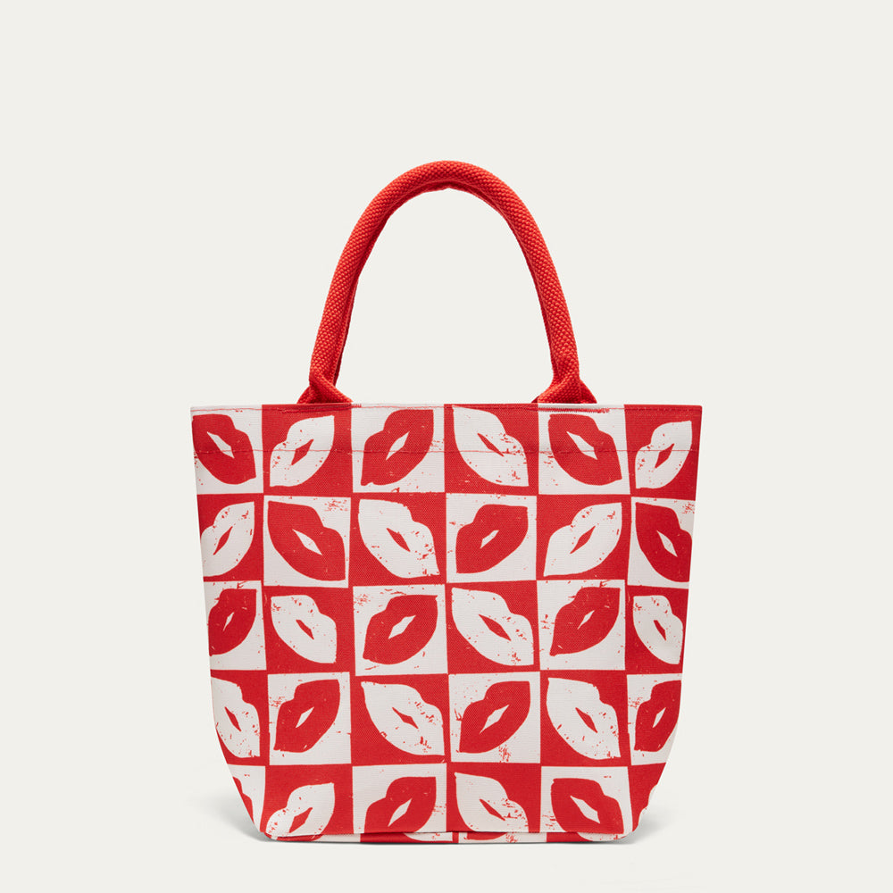 A red and white patterned tote bag with red rope handles, featuring a repeating print of lips in red and white on a light gray background.