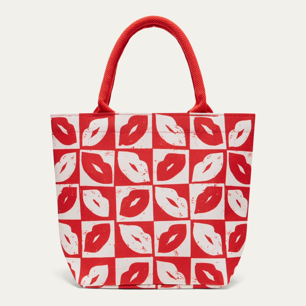 A red and white patterned tote bag with red rope handles, featuring a repeating print of lips in red and white on a light gray background.