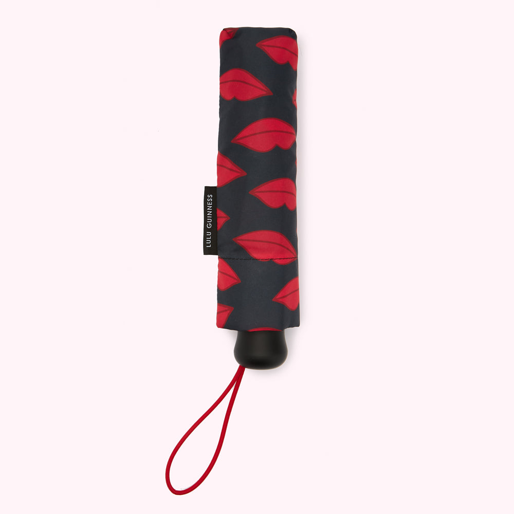 A closed Lulu Guinness compact umbrella with a dark-grey background and a red lips pattern.