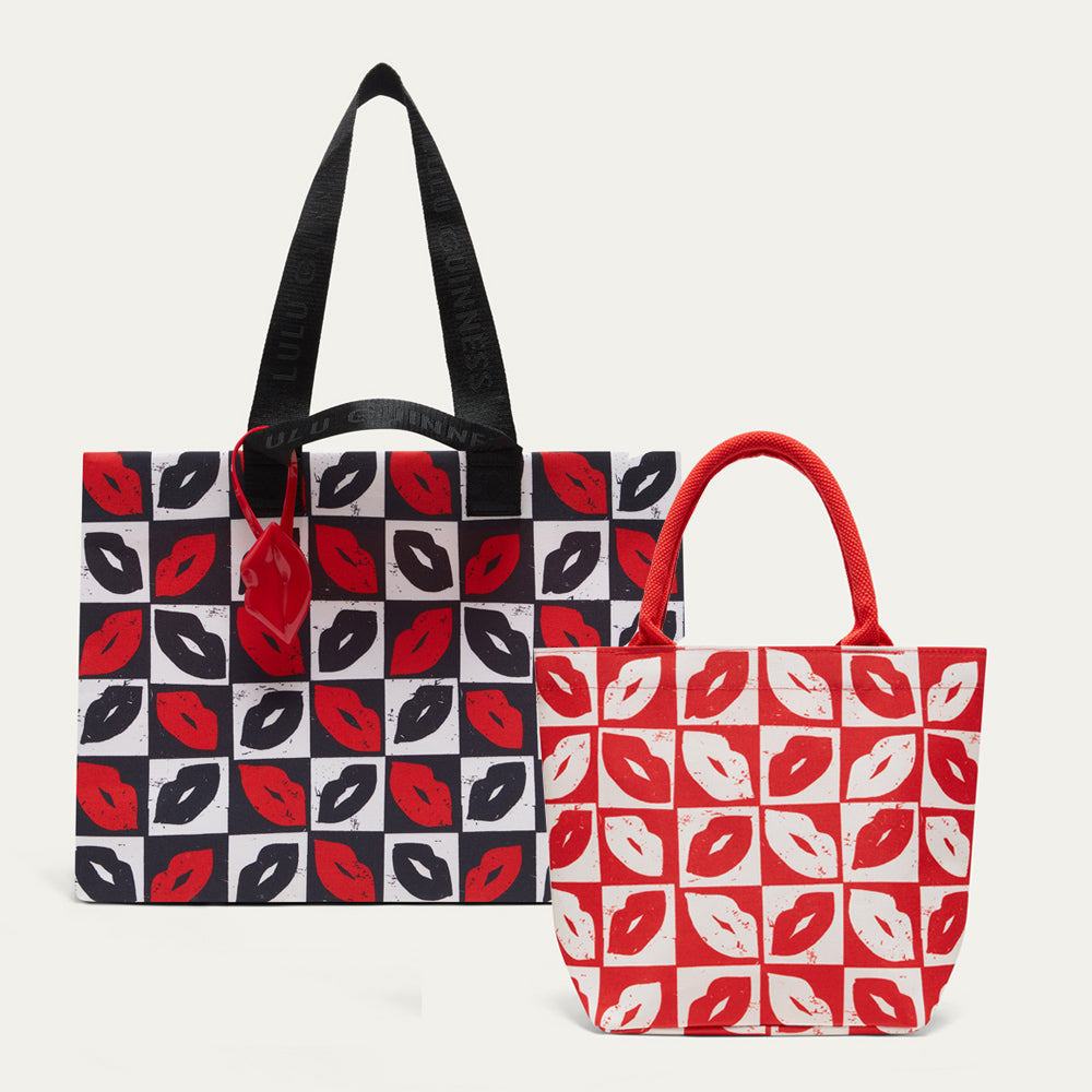 Two tote bags with a lip print pattern, one black and red and one red and white, displayed against a light gray background.