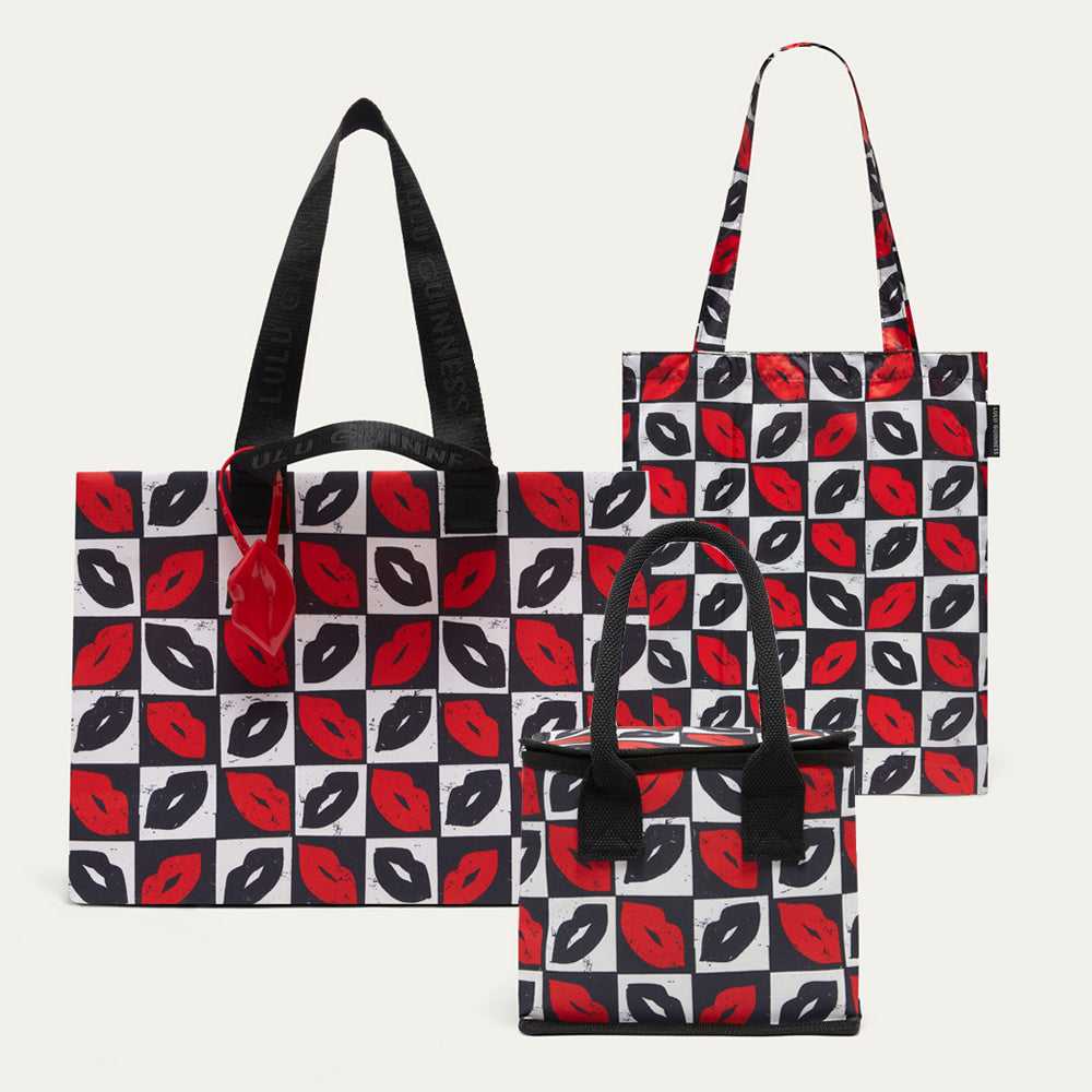 Three tote bags with black handles, featuring a repeating red and black lips pattern on a white background, displayed against a light gray studio backdrop.