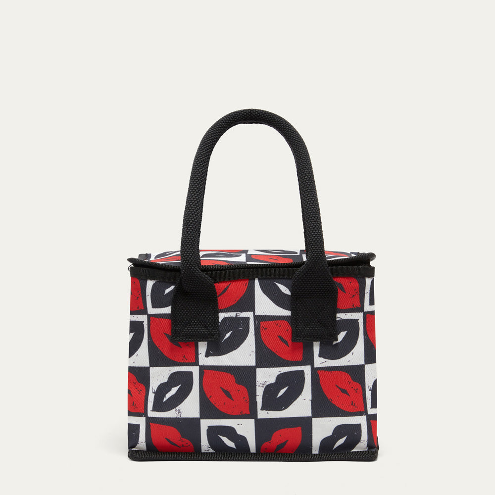 A square lunch bag with black handles, featuring a black, white, and red checkerboard pattern of lips on the front, set against a plain light beige background.