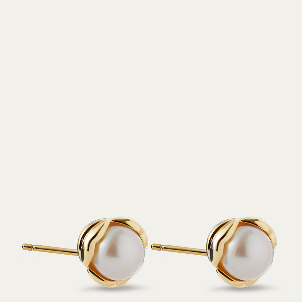 Pair of gold stud earrings with white pearls on a light beige background