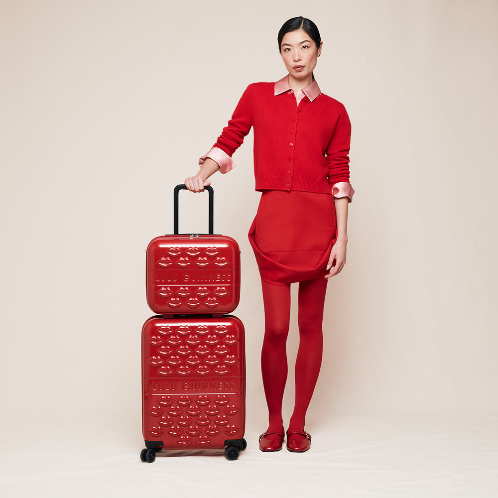 Woman in a red outfit holding a matching red suitcase against a beige background