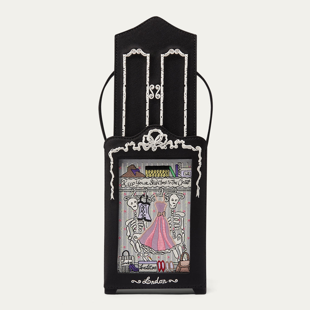 A black gothic-style wardrobe-shaped handbag with sliding doors revealing embroidered skeletons in the closet, shown against a plain light background.