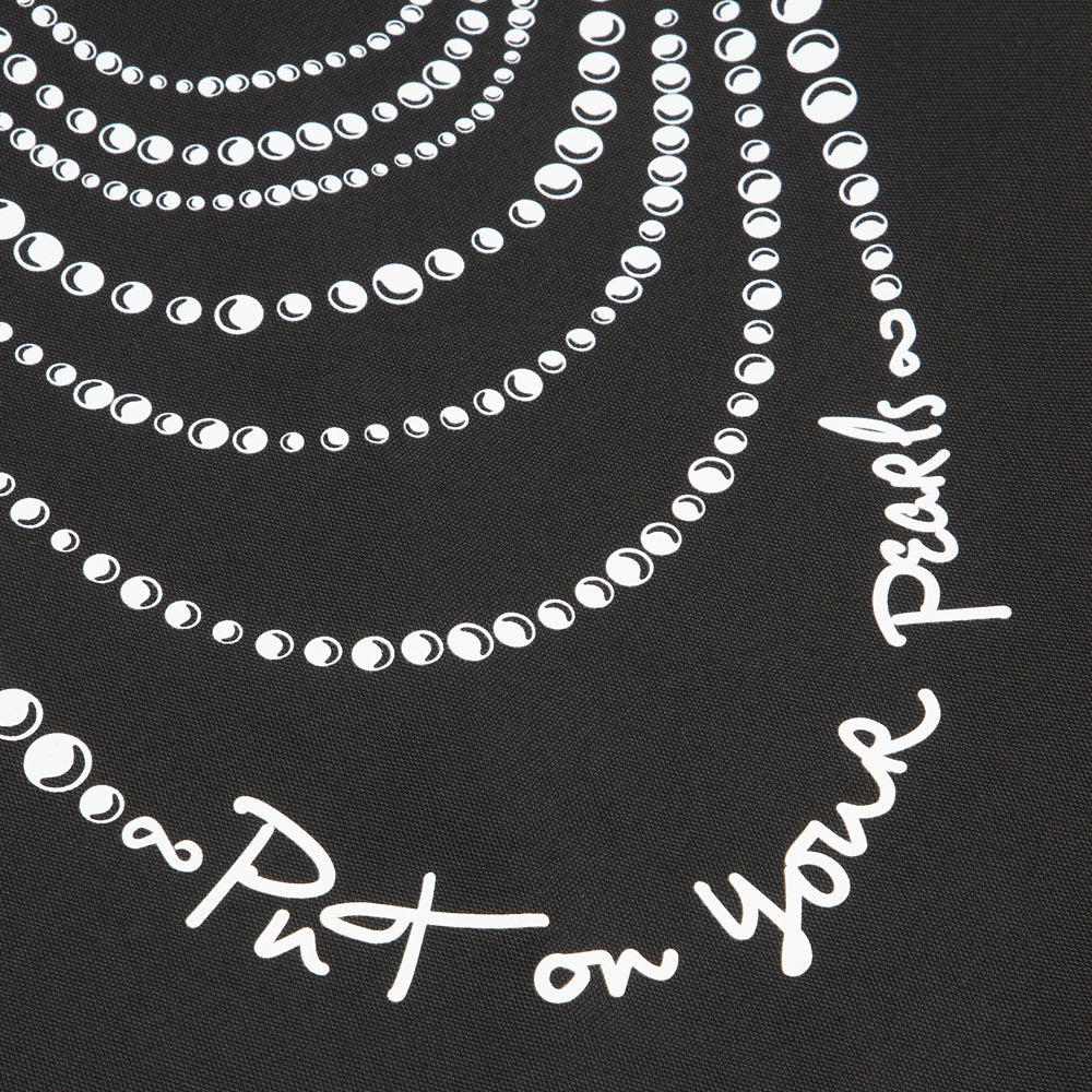 Close-up of a black textile with a design of white pearl necklaces and the text "Put on your Pearls".
