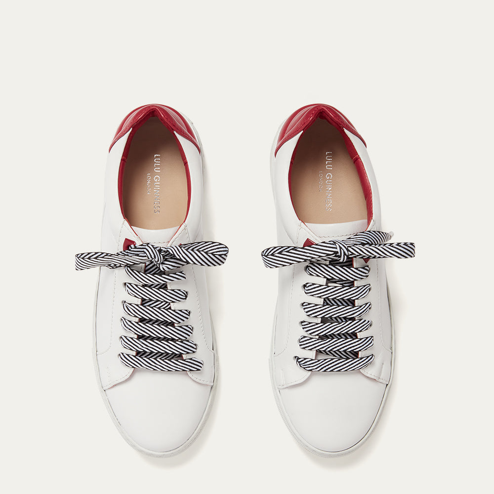 White sneakers with red soles and striped laces on a light gray background