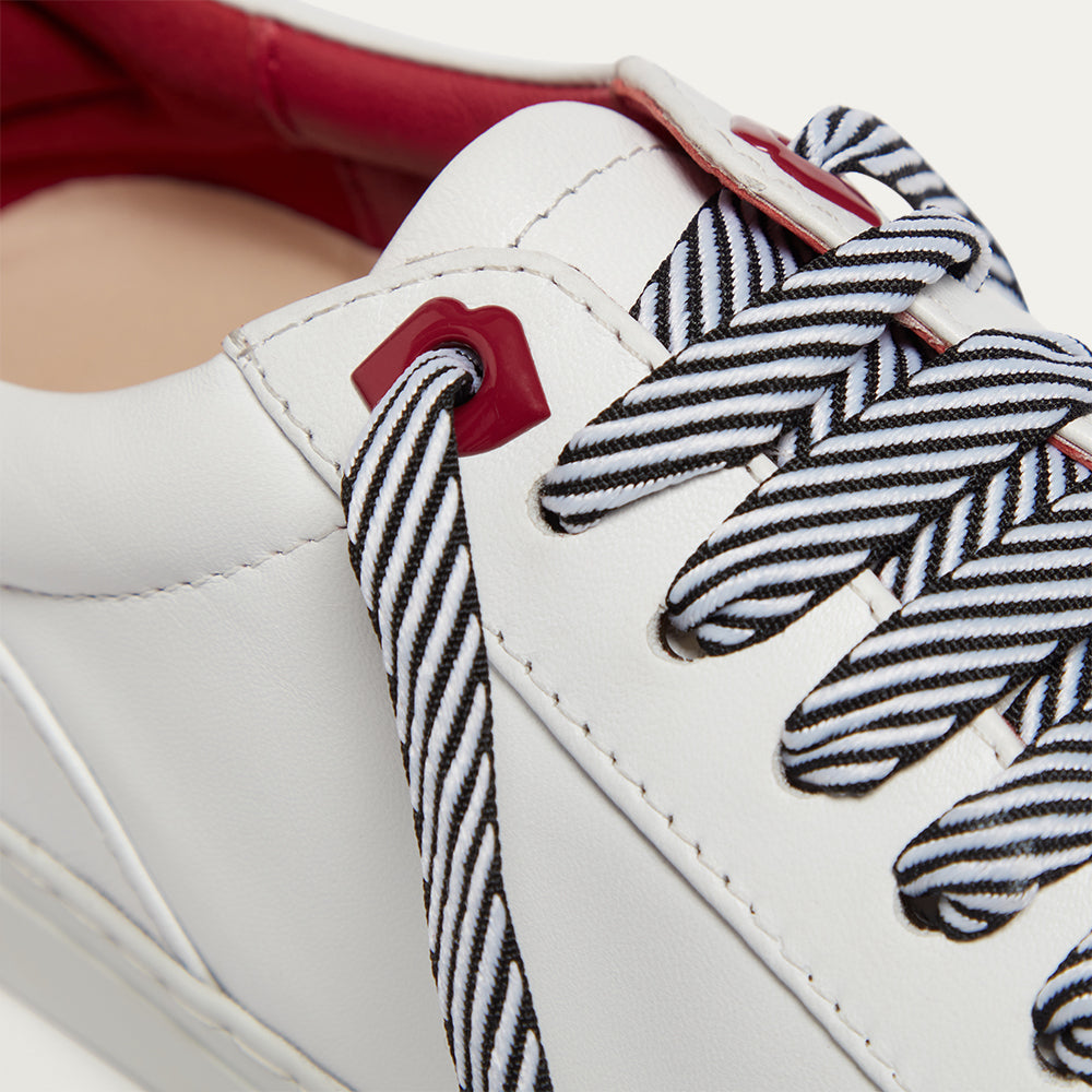 Close-up of a white sneaker with black and white striped laces and a red lip shaped eyelets.