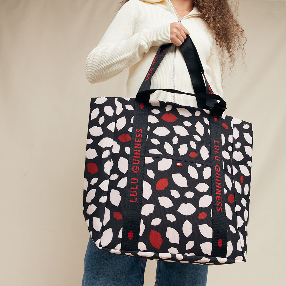 Person holding a Lulu Guinness tote bag with a lip patterned design on a beige background