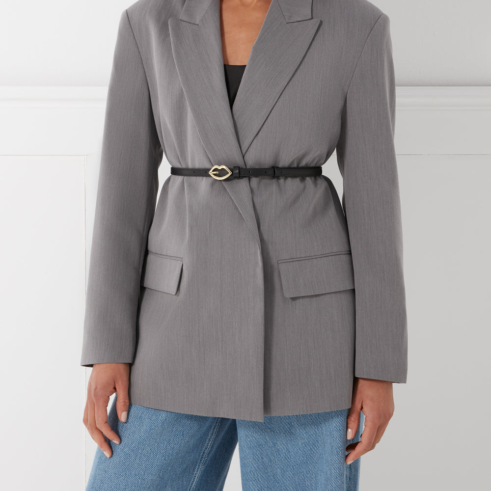 A grey blazer cinched with a thin black belt featuring a gold lip-shaped buckle over light blue jeans.
