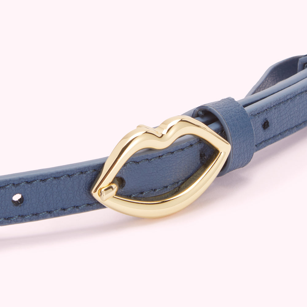 Close-up of a blue leather belt with a gold lip-shaped buckle.
