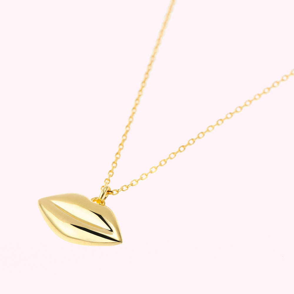 Gold necklace with a lip-shaped pendant against a white background.
