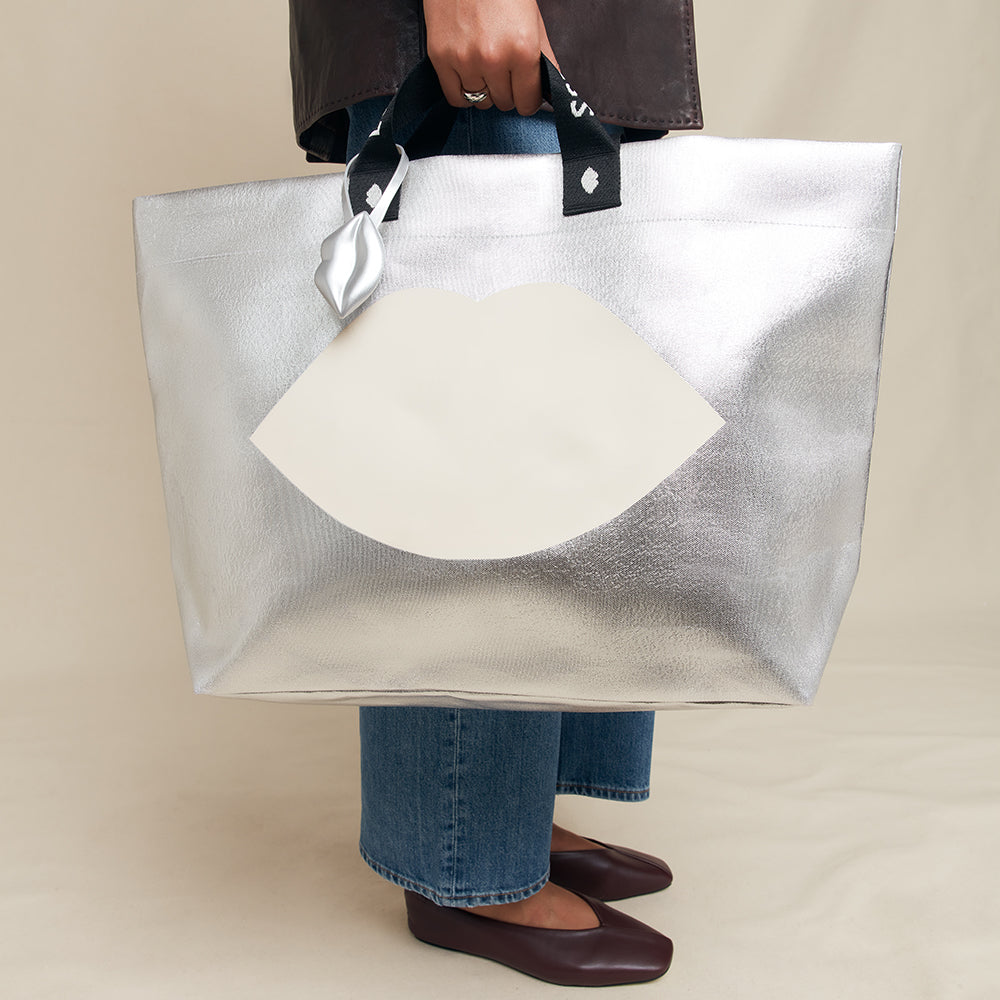 Person holding a large silver tote bag with a lip print against a neutral background