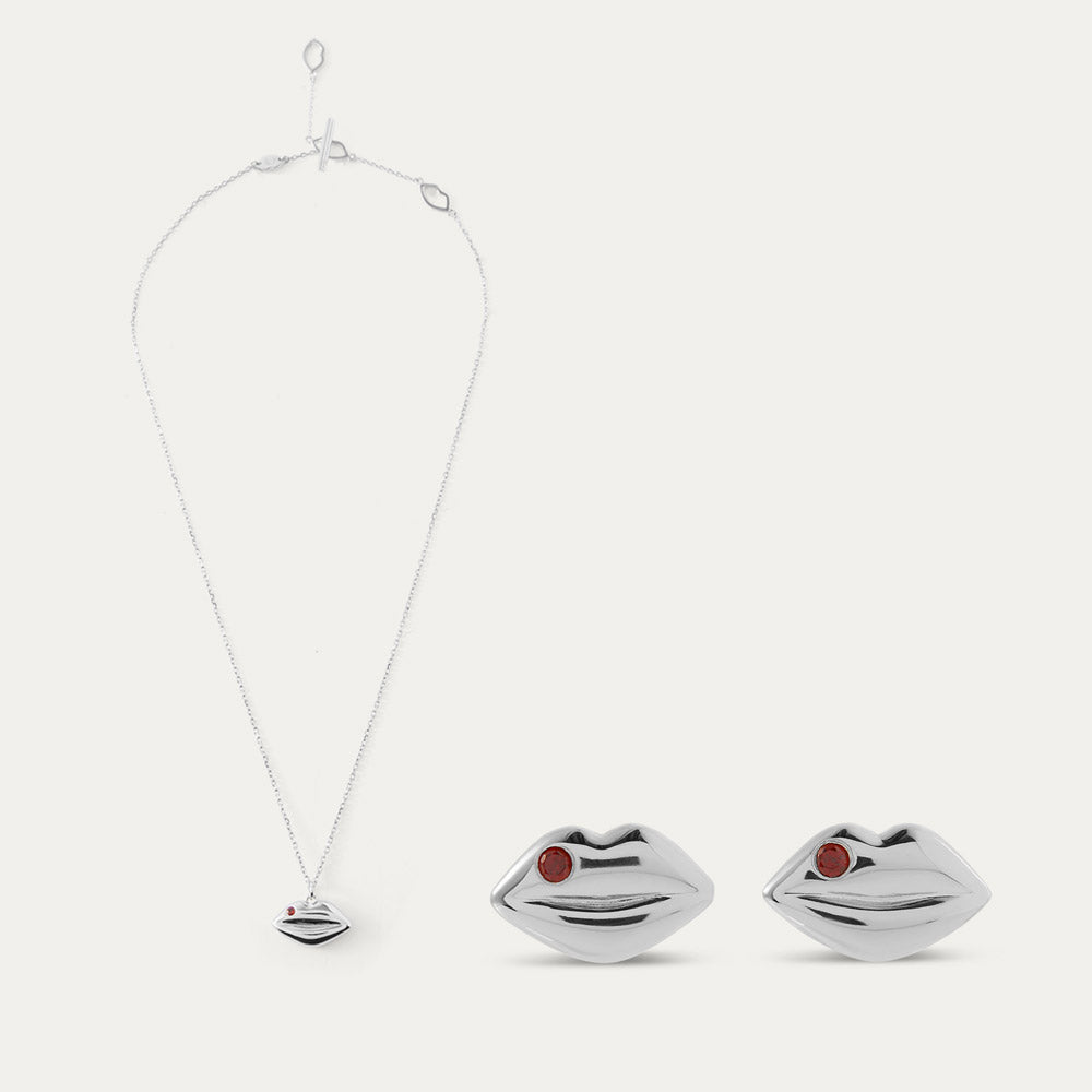 Silver lip-shaped pendant and earrings with red stones on a white background