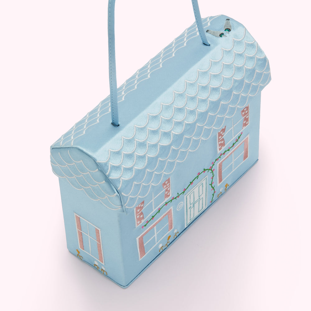 A light blue handbag shaped like a house with an embroidered roof and details.