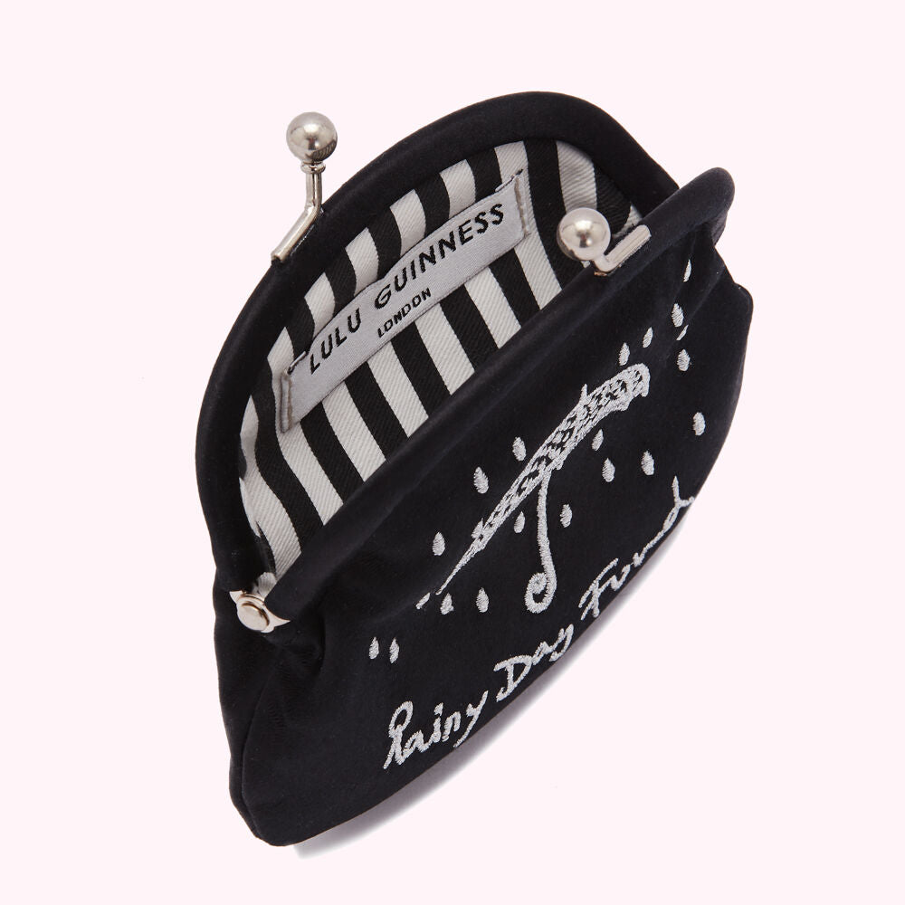 Black Lulu Guinness purse open to reveal a black and white striped interior; the purse is embroidered with an umbrella and the words "Rainy Day Fund".
