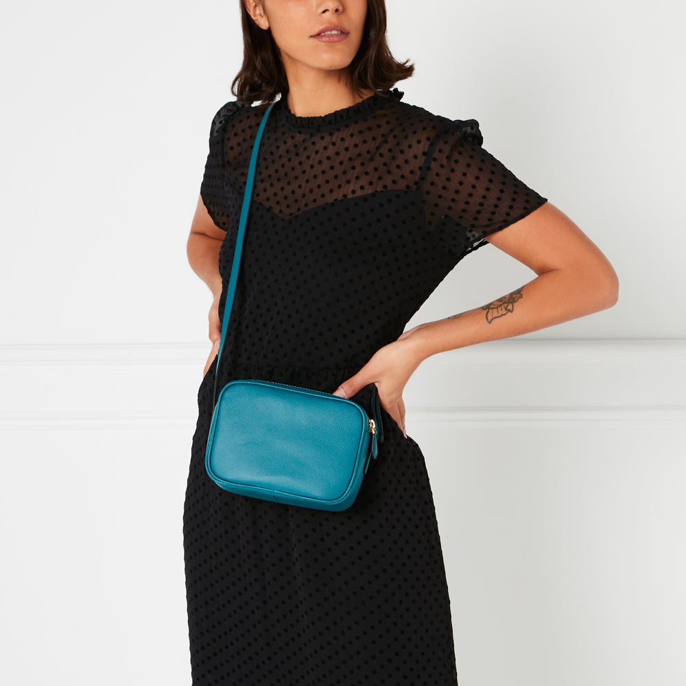 Woman in black polka dot dress carrying a teal crossbody bag.
