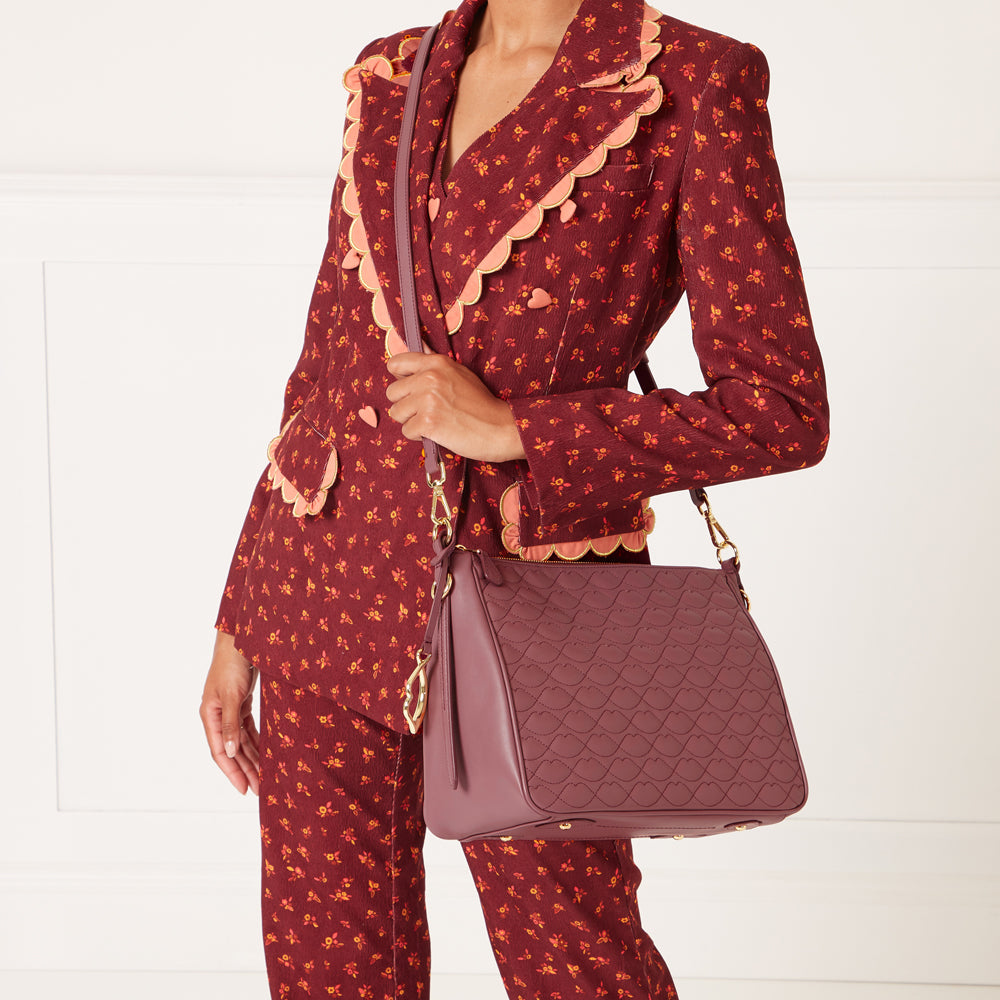 A mauve quilted handbag with a long strap slung over the shoulder of a model wearing a burgundy floral suit.