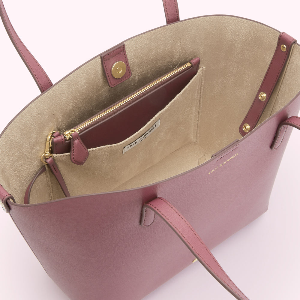 Inside of a dusty rose Lulu Guinness tote bag showing a beige interior and a zippered pocket.
