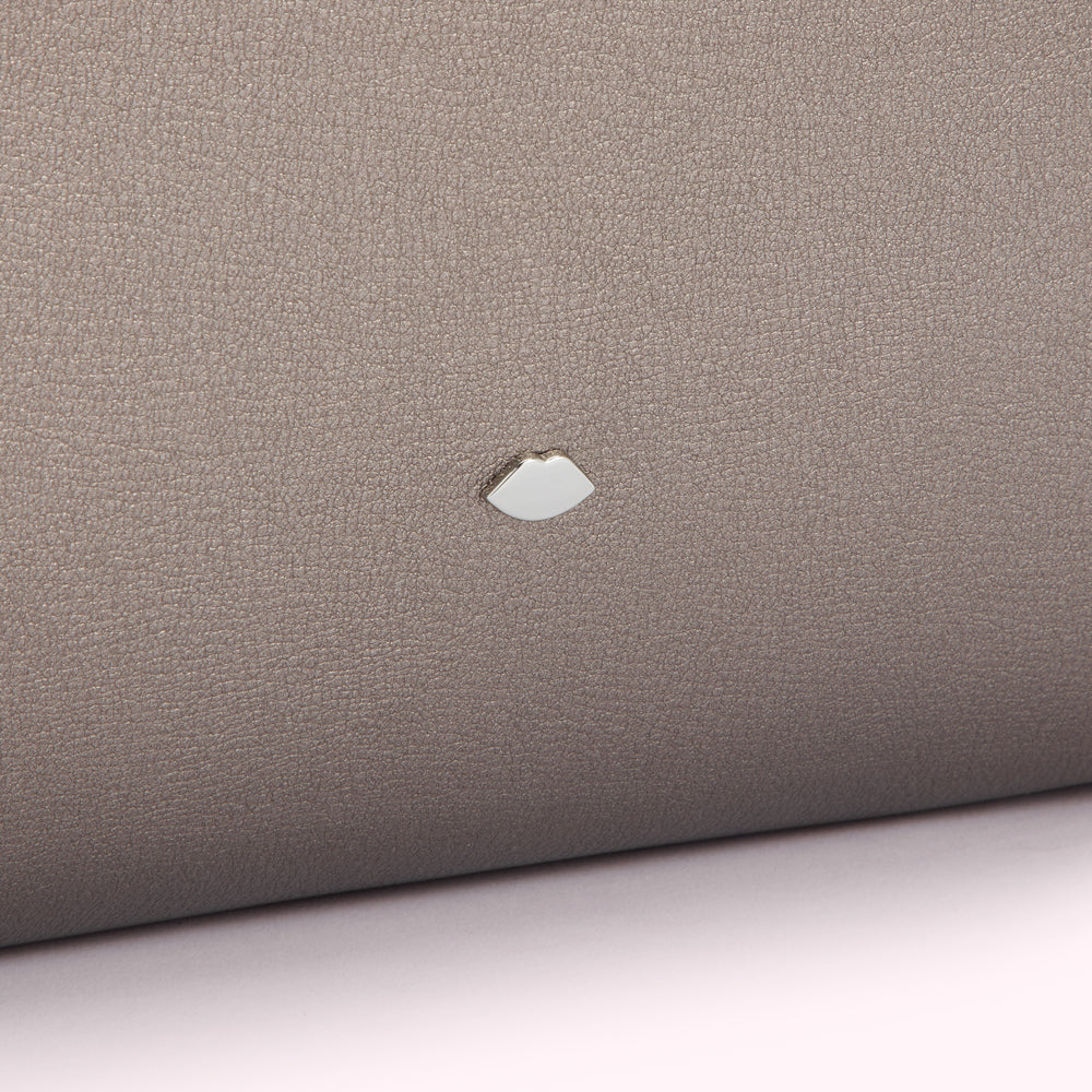 Close-up of a taupe-coloured leather surface with a small, metallic lip-shaped logo.
