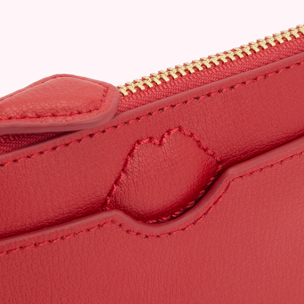Close-up of a red leather purse with a gold zipper and a heart-shaped detail.
