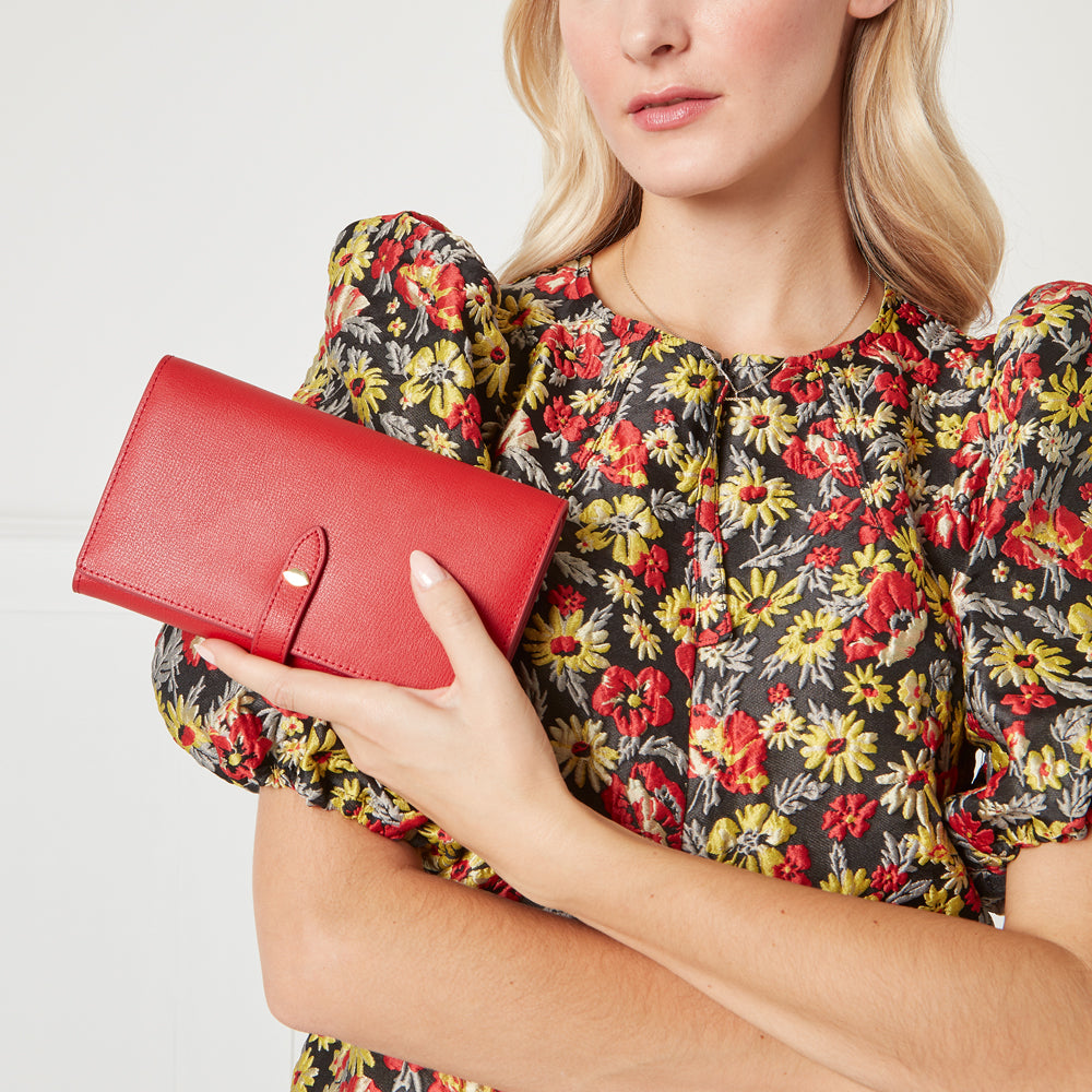Woman in floral dress holding a red leather wallet.
