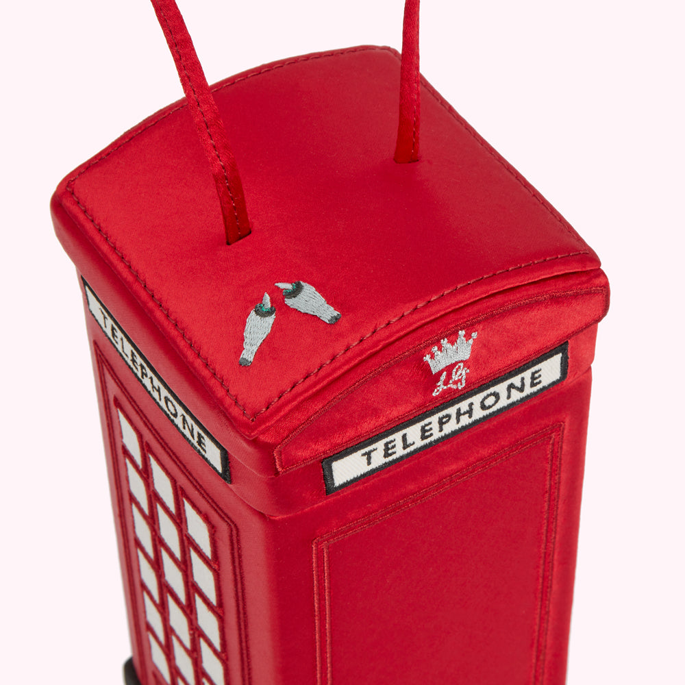 Close-up of a red satin handbag shaped like a British telephone box, featuring embroidered details.
