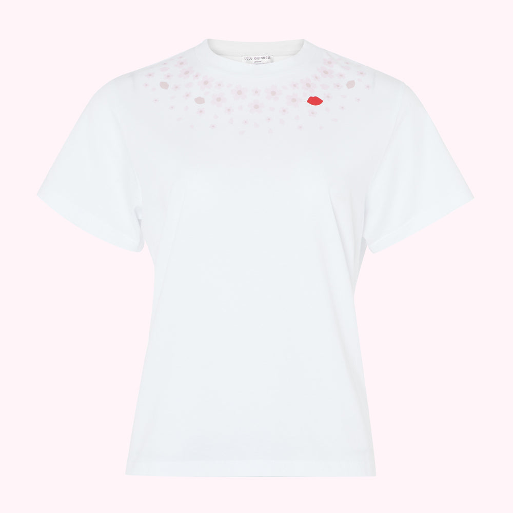White short-sleeved t-shirt with pink cherry blossom and red lip print near neckline against pink background.
