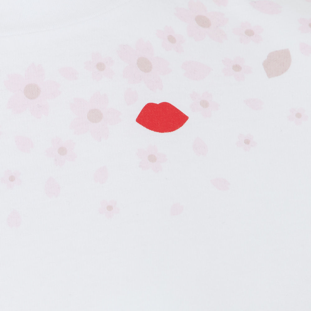 White background with scattered light pink flowers and a single red lipstick in the centre.