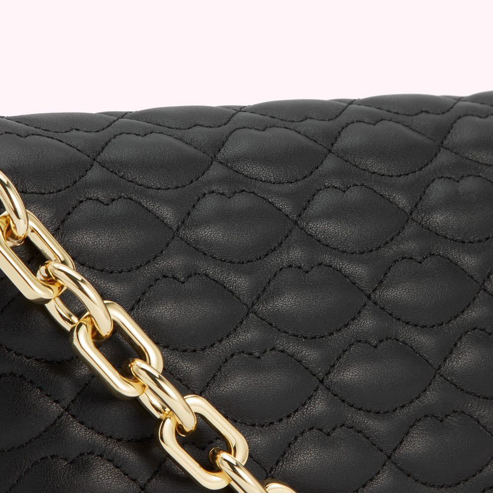 Close-up of a black quilted handbag with a gold chain strap; the quilting is shaped like lips.
